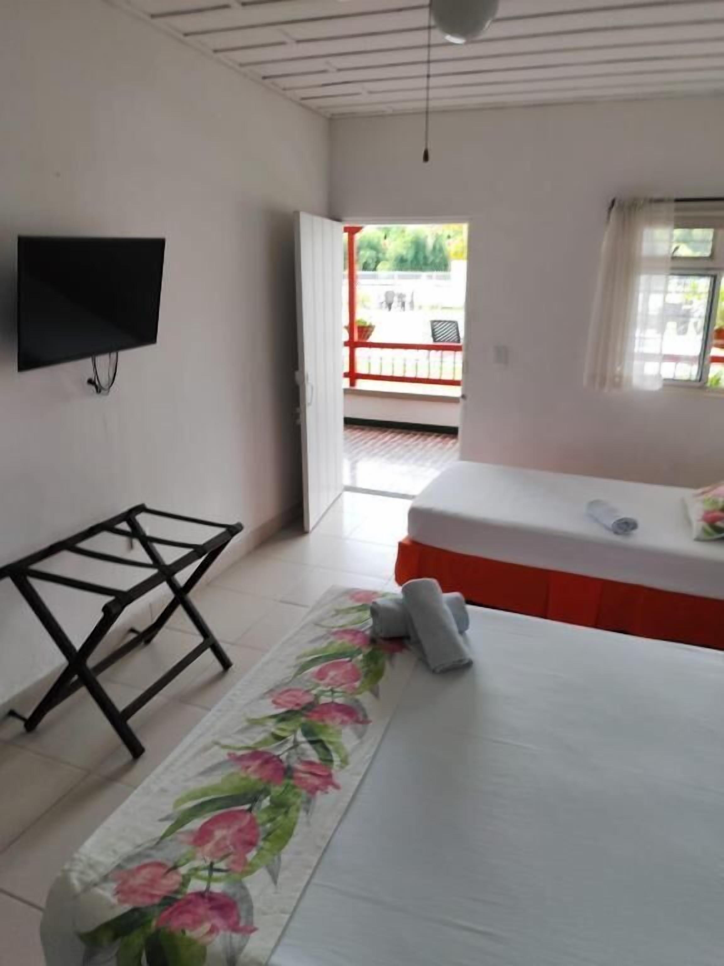 Un dormitorio con cama, televisor montado en la pared, ventana y balcón visible a través de una puerta abierta.
