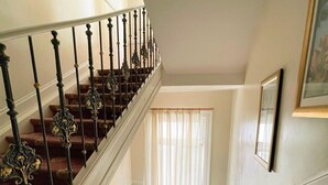 Een trap met versierde zwarte balustrades en rode, tapijtbeglazing, die naar een plateau leidt.