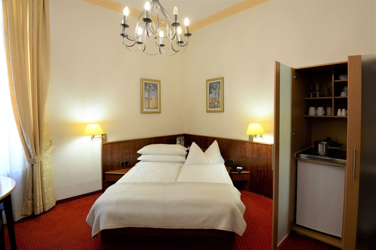 Une chambre d’hôtel avec un grand lit, deux tables de chevet avec des lampes, une armoire en bois et un lustre.