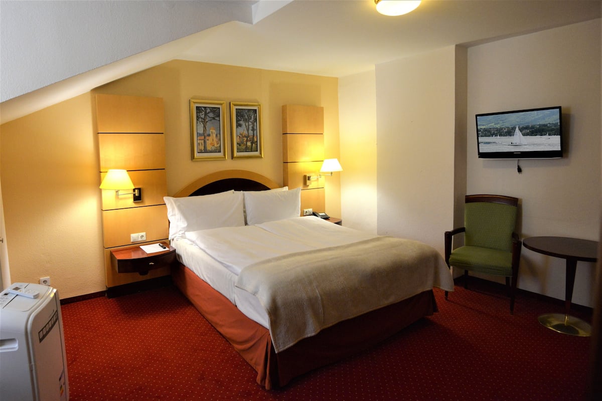 Une chambre d’hôtel comprenant un lit, deux lampes de chevet, une télévision, une chaise et une petite table.