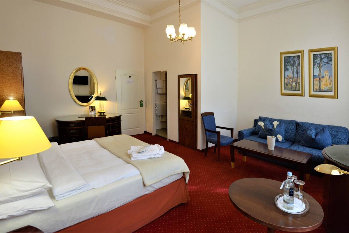 Une chambre d’hôtel comprenant un lit, un canapé, une table basse, un miroir et un lustre.