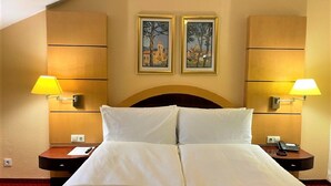 Een hotelkamer met een groot bed, twee nachtkastjes, een houten hoofdbord, twee wandlampen en twee ingelijste foto’s boven het bed.