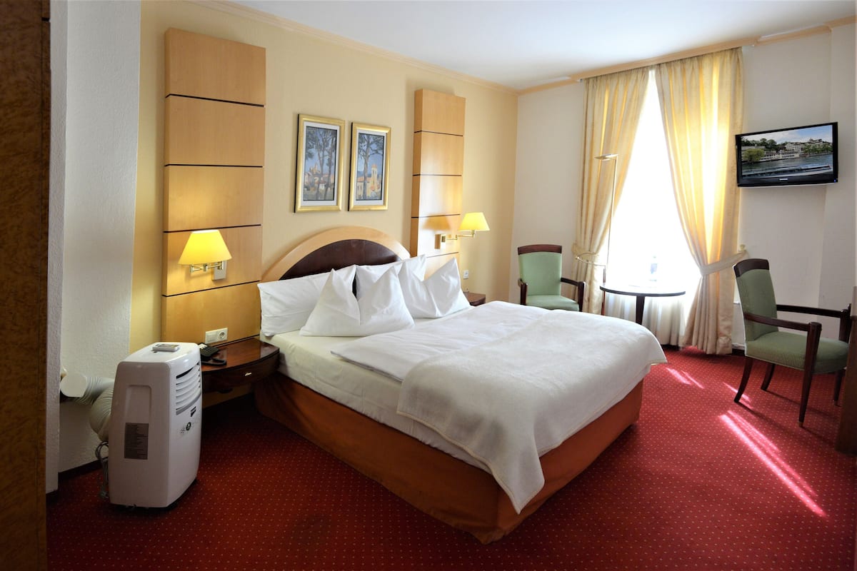 Une chambre d’hôtel avec un grand lit, deux lampes de chevet, un téléviseur à écran plat, un bureau avec une chaise et une fenêtre avec des rideaux.