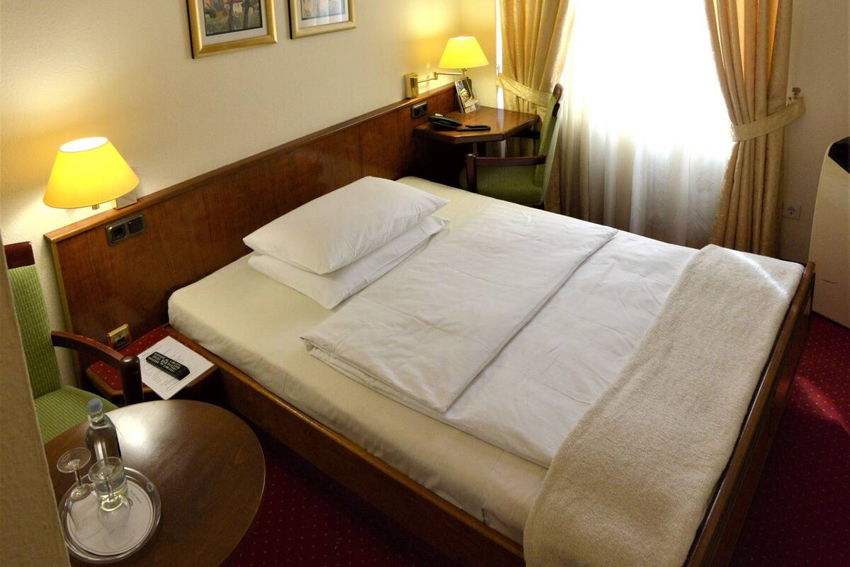 Une chambre d’hôtel avec un lit bien fait, deux lampes de chevet, une petite table avec un verre et une chaise.