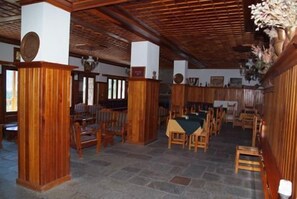 A spacious room with wooden pillars, stone flooring, and a dining area with tables and chairs.