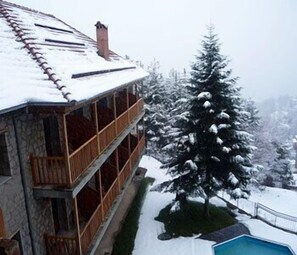 A multi-story building with a stone facade, wooden balconies, and a snow-covered roof. - Victoria (Metsovo)