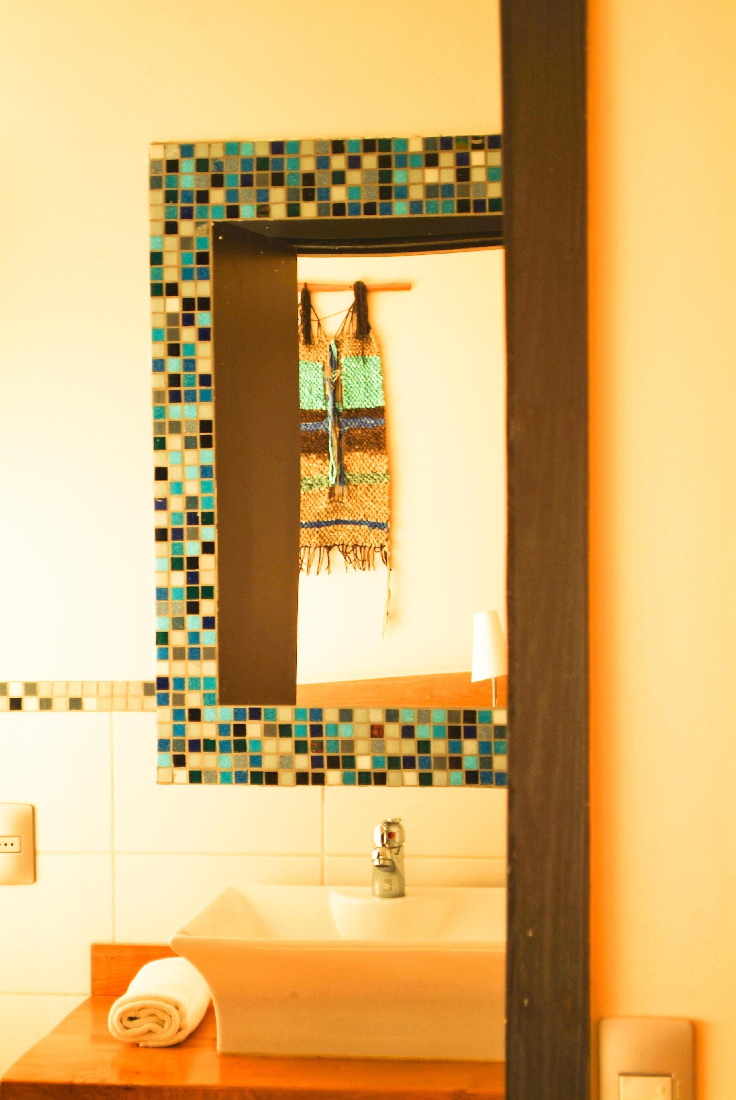 A bathroom with a tiled wall, a sink, a towel, and a mirror.