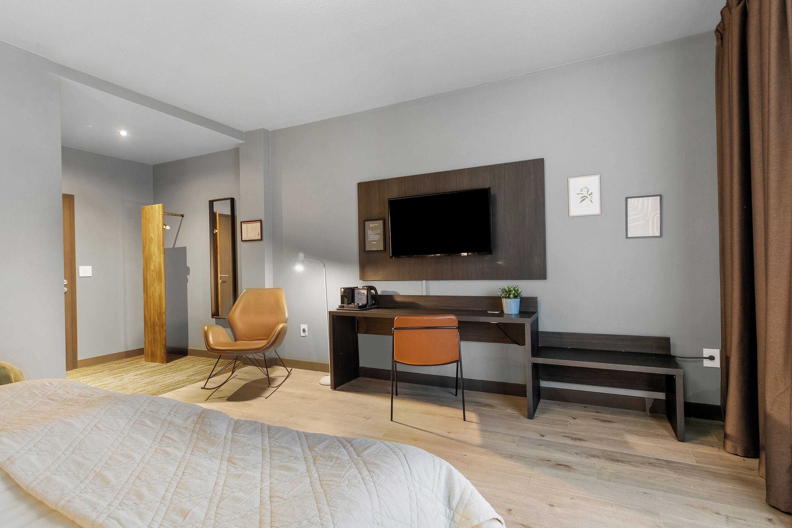 Une chambre d’hôtel moderne dotée d’un grand lit, d’un bureau avec une chaise, d’une télévision à écran plat et d’un petit banc.