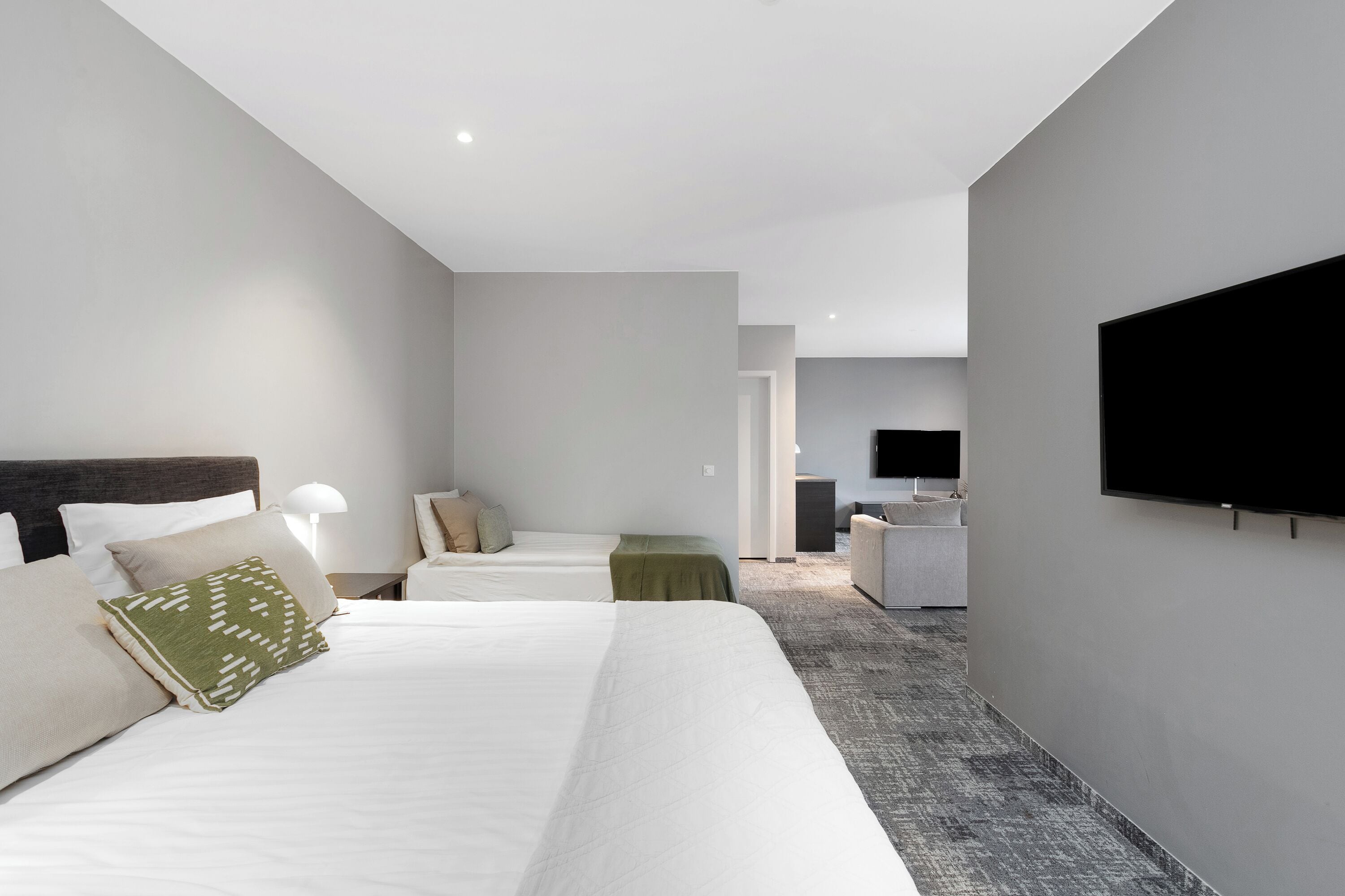 A modern hotel room with two beds, a flat-screen TV, and a small seating area.