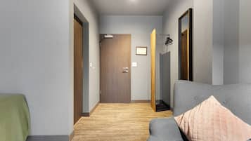 Ein moderner Flur mit einer Holztür, einem grauen Sofa mit gestepptem Kissen und einem Holzboden.