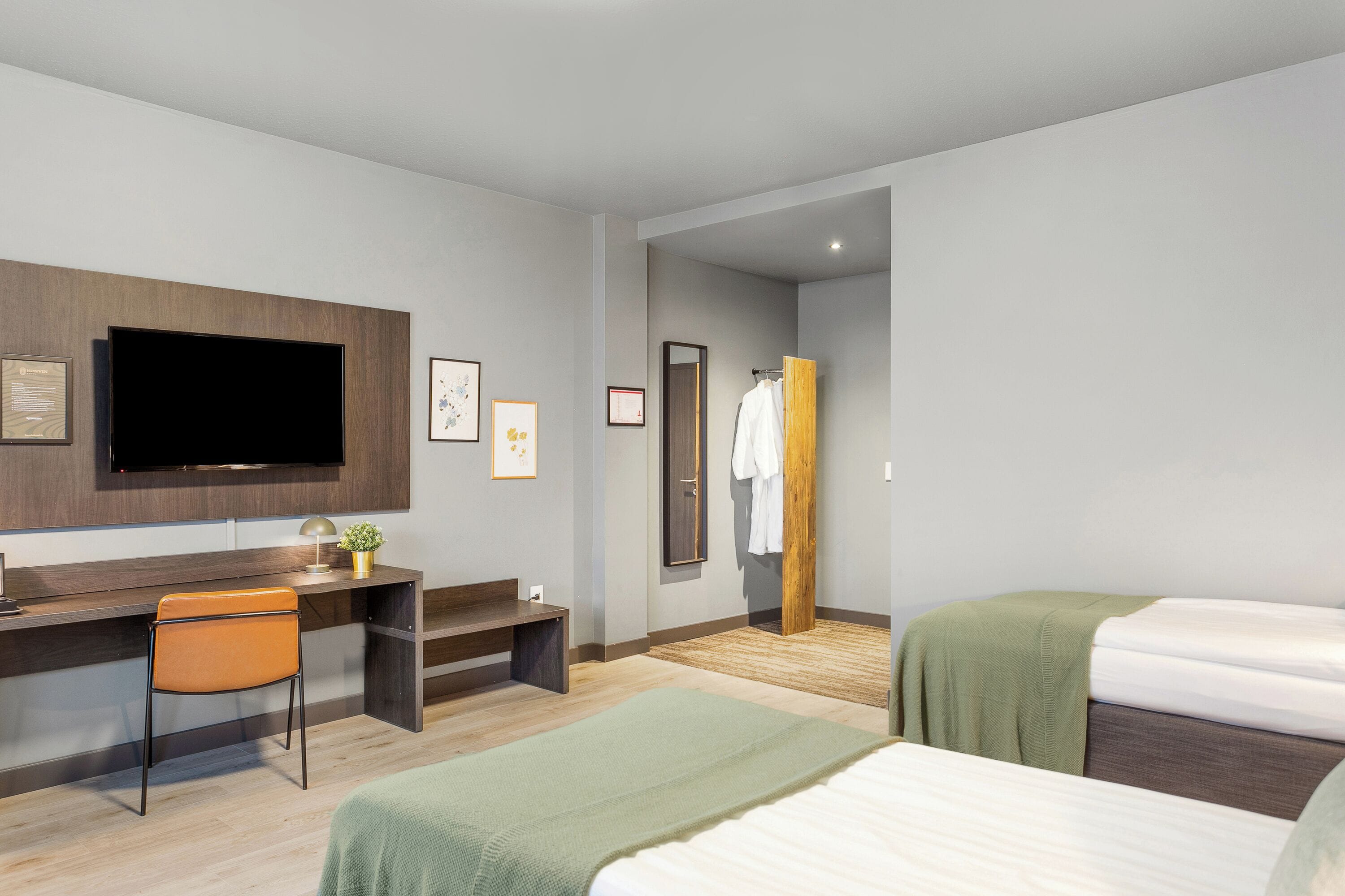 Una moderna camera d'albergo con TV a schermo piatto, una scrivania con sedia, due letti e una porta in legno.