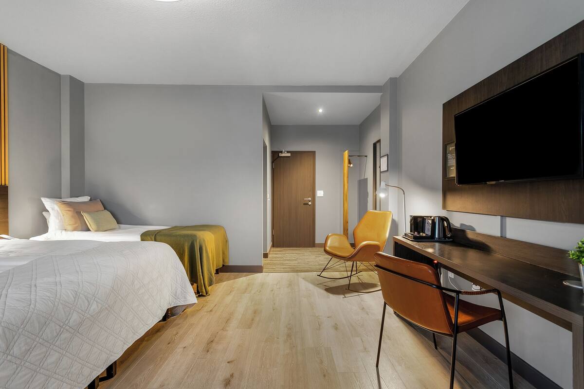 A hotel room with a bed, a desk, a chair, a television, and a door leading to another room.