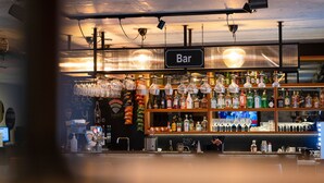A bar area with a 'Bar' sign, shelves of liquor bottles, and hanging glasses. - Konvin Hotel by Reykjavik Keflavik Airport (Reykjanesbær)