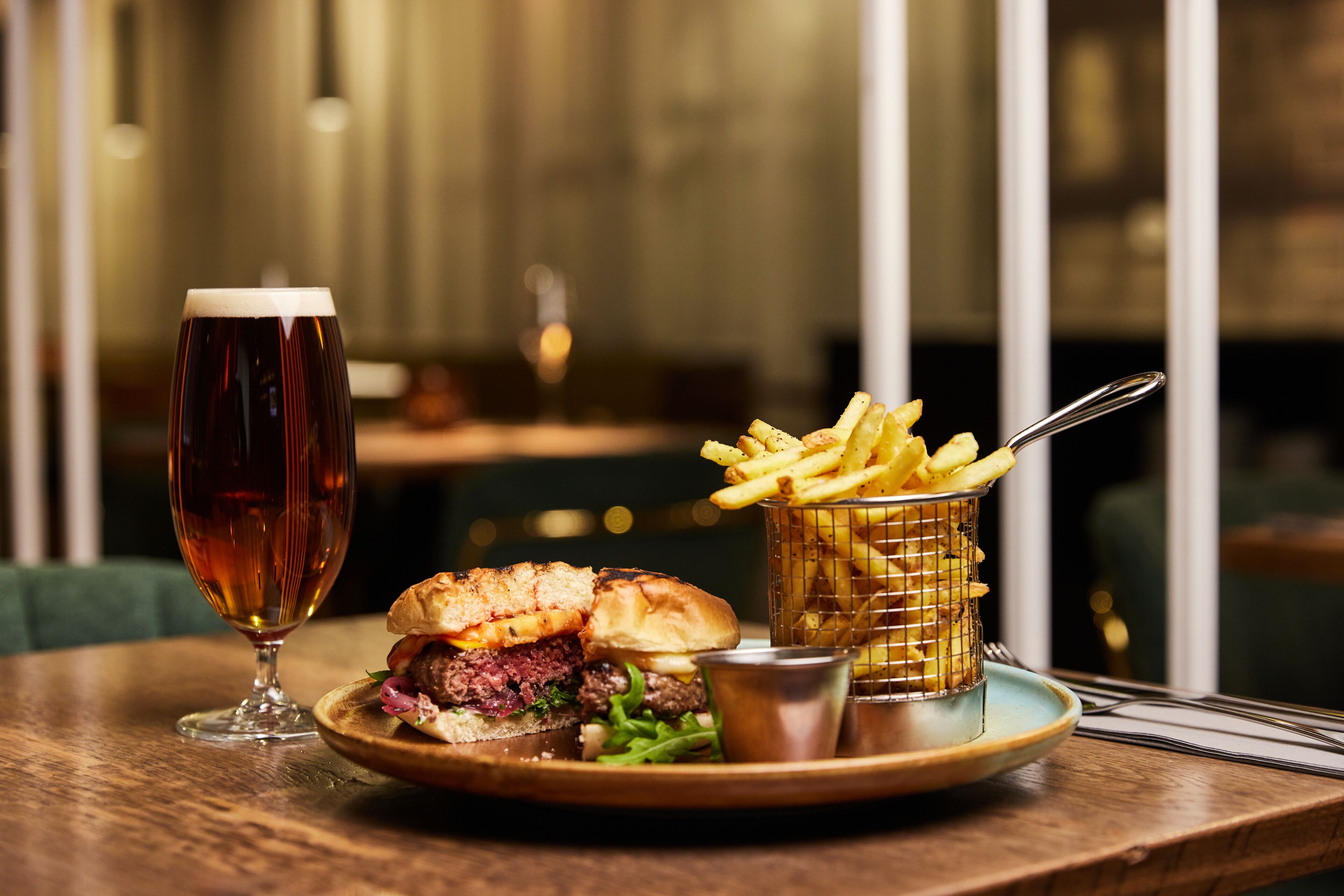 A meal consisting of a burger, fries, and a beer on a wooden table.