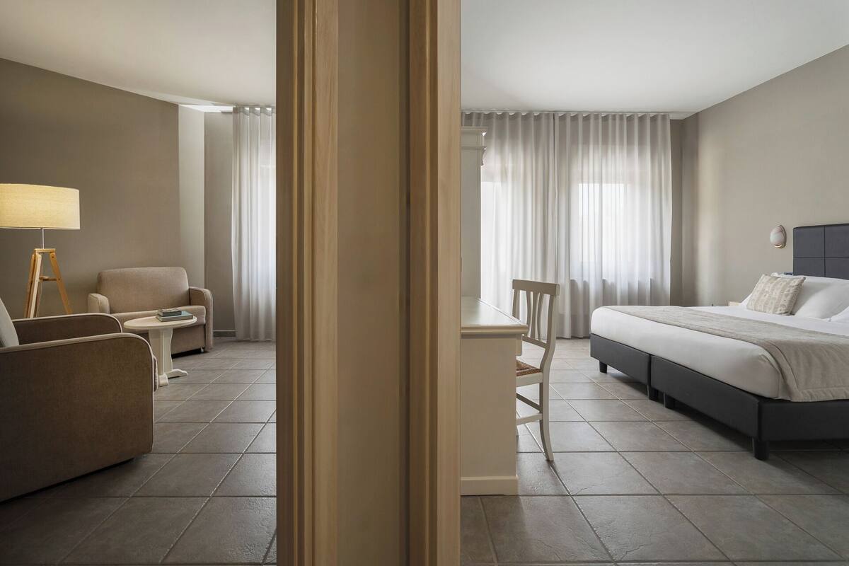 A hotel room with a bed, a chair, a small table, and a lamp.