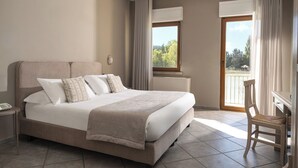 A hotel room with a large bed, a desk, and a view of a balcony with trees and a body of water. - Hotel Don Luis (Castel di Sangro)