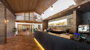 A spacious lobby with a high ceiling, a bar area with a stone wall, and a wooden reception desk. - Hotel Don Luis (Castel di Sangro)