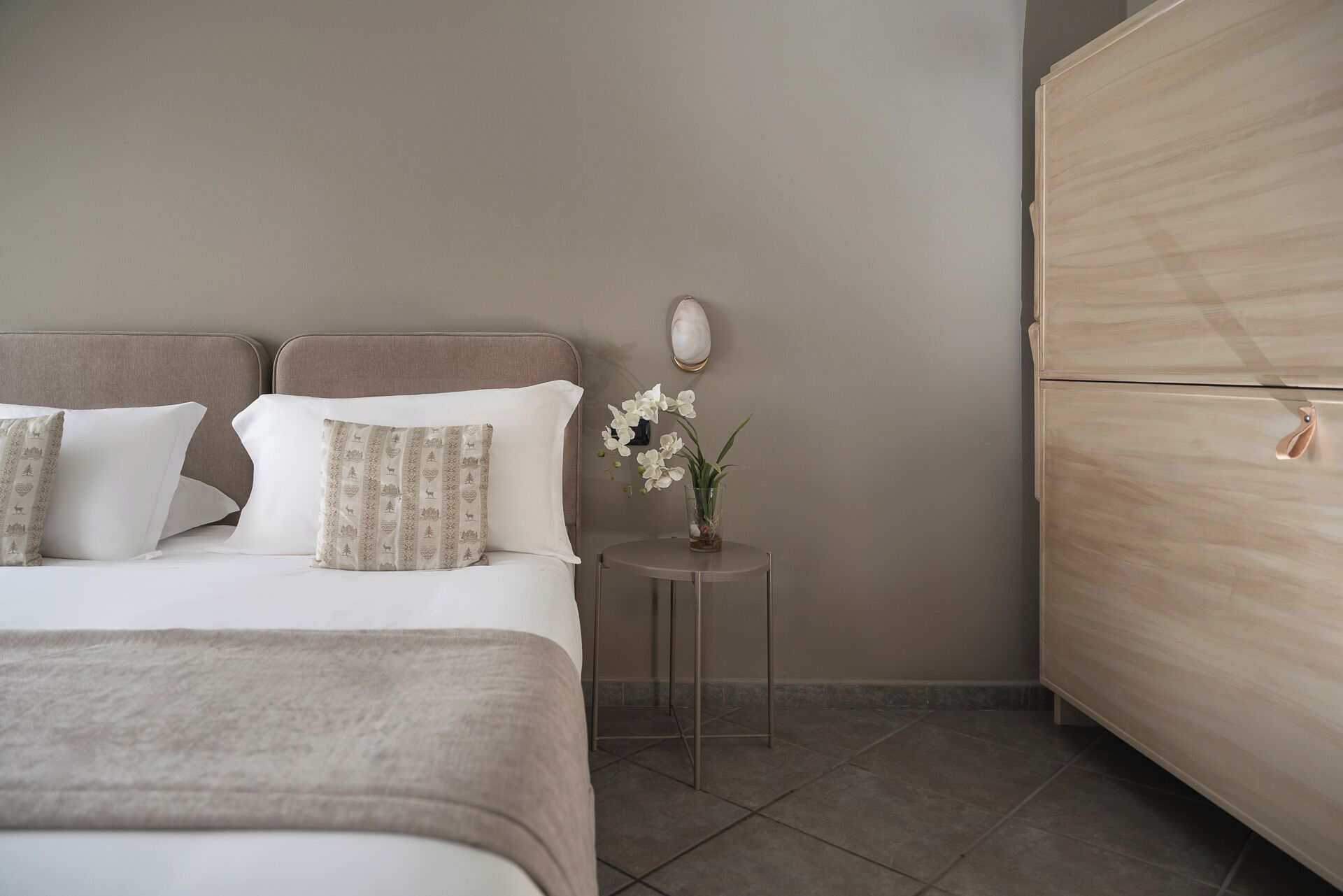 A bedroom with a bed, pillows, a bedside table with a vase of flowers, and a wardrobe.