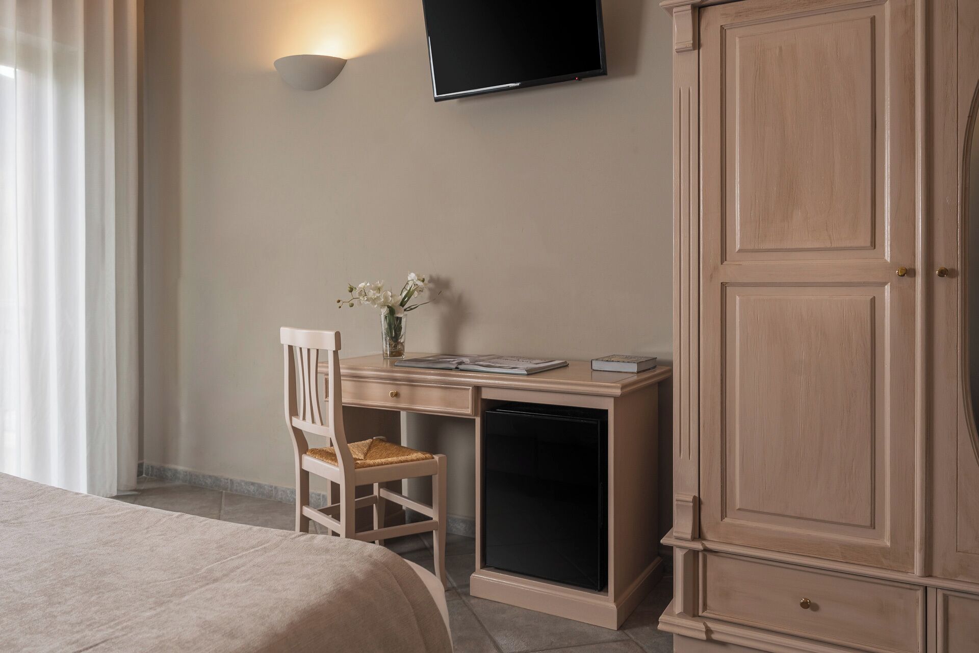 A hotel room with a bed, a desk with a chair, a TV mounted on the wall, and a wardrobe.