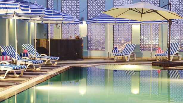 An indoor swimming pool with striped lounge chairs and umbrellas, surrounded by patterned glass walls. - Rayan Hotel Sharjah (Sharjah)