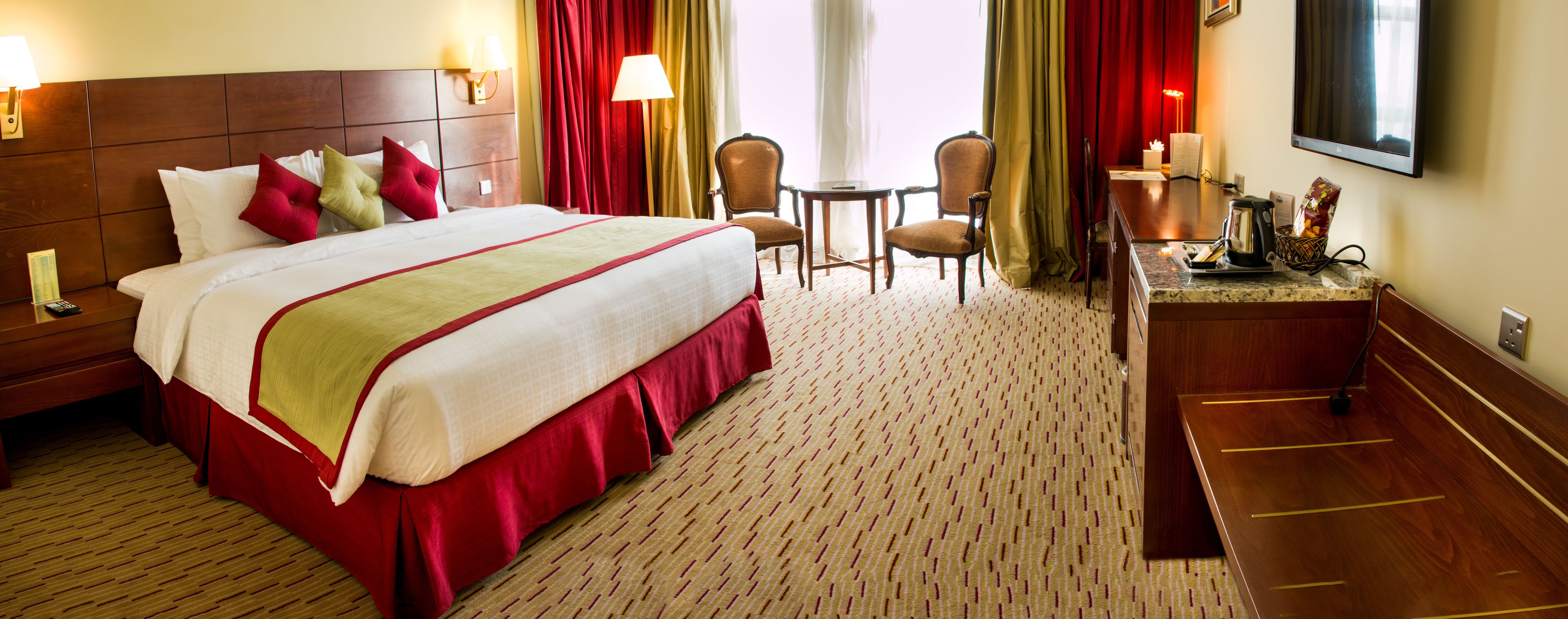 Ein Hotelzimmer mit einem großen Bett, einem Schreibtisch, zwei Stühlen, einem Fernseher und einer Kaffeemaschine.