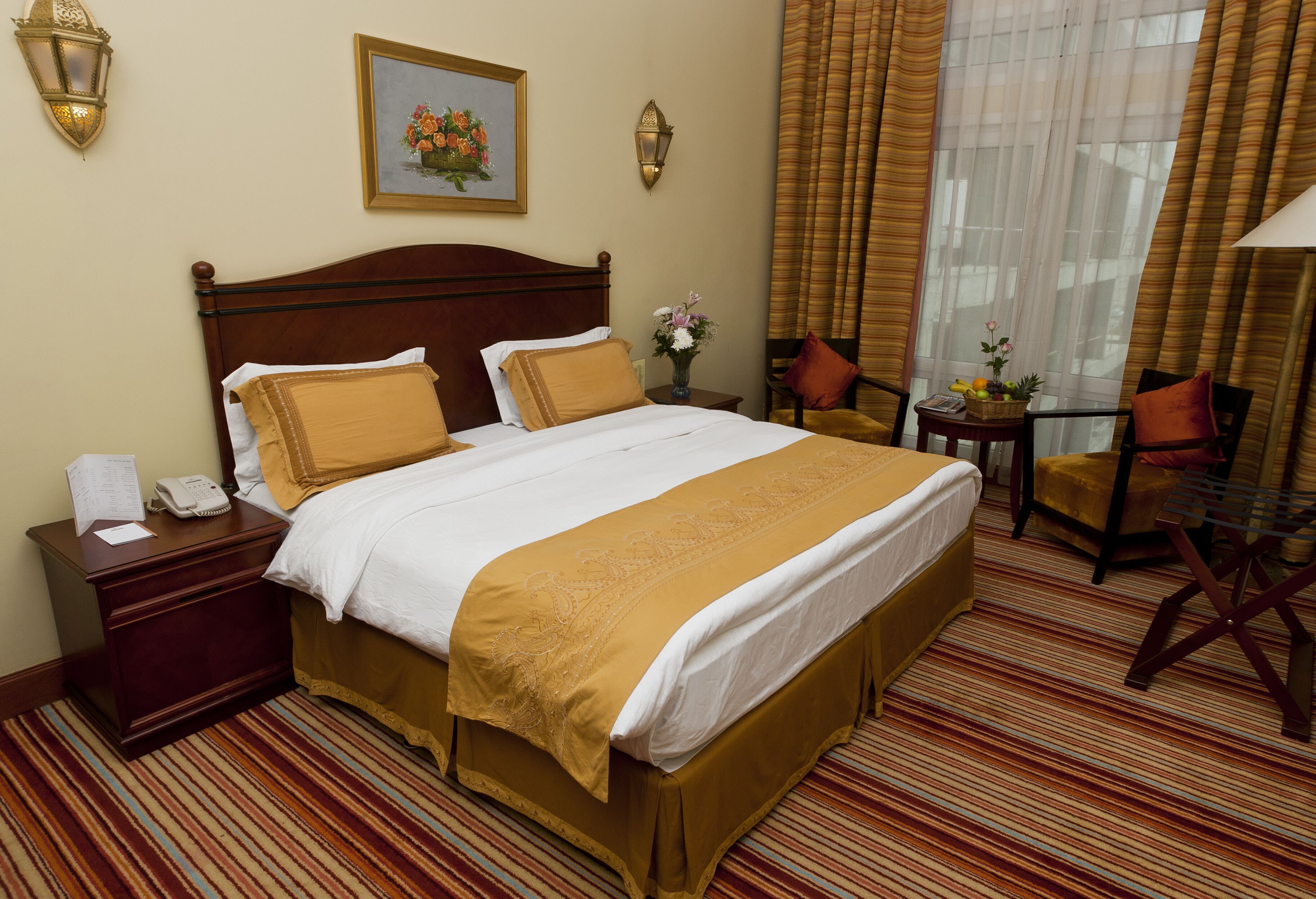 A hotel room with a large bed, a nightstand with a telephone, a small table with a vase of flowers, and a chair.