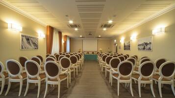 A conference room with rows of chairs, a projector screen, and wall-mounted lights.