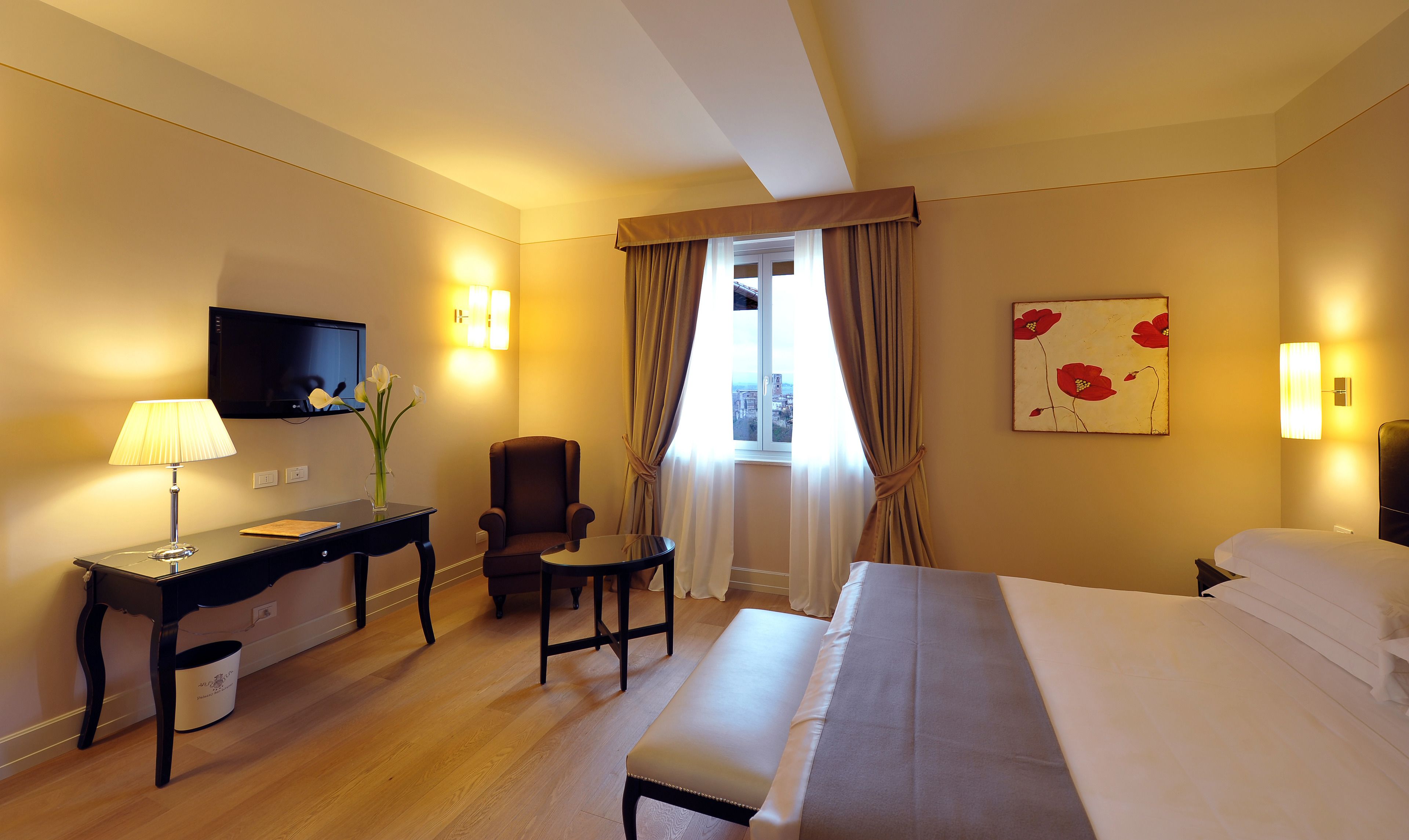Une chambre d’hôtel avec un lit, un bureau avec une lampe, une chaise, un téléviseur fixé au mur et une fenêtre avec des rideaux.