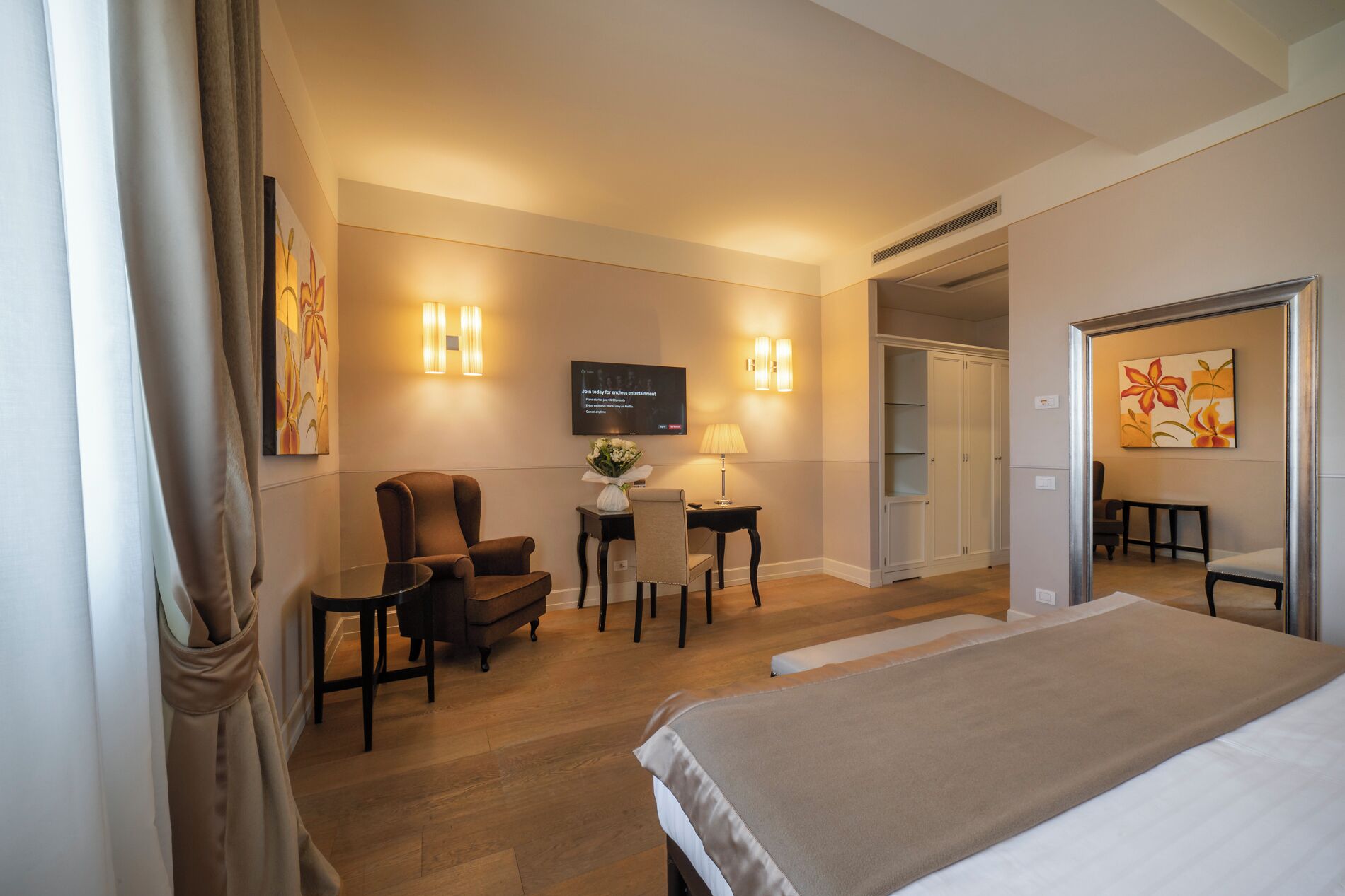 A hotel room with a bed, a desk with a chair, a television, and a door leading to another room.