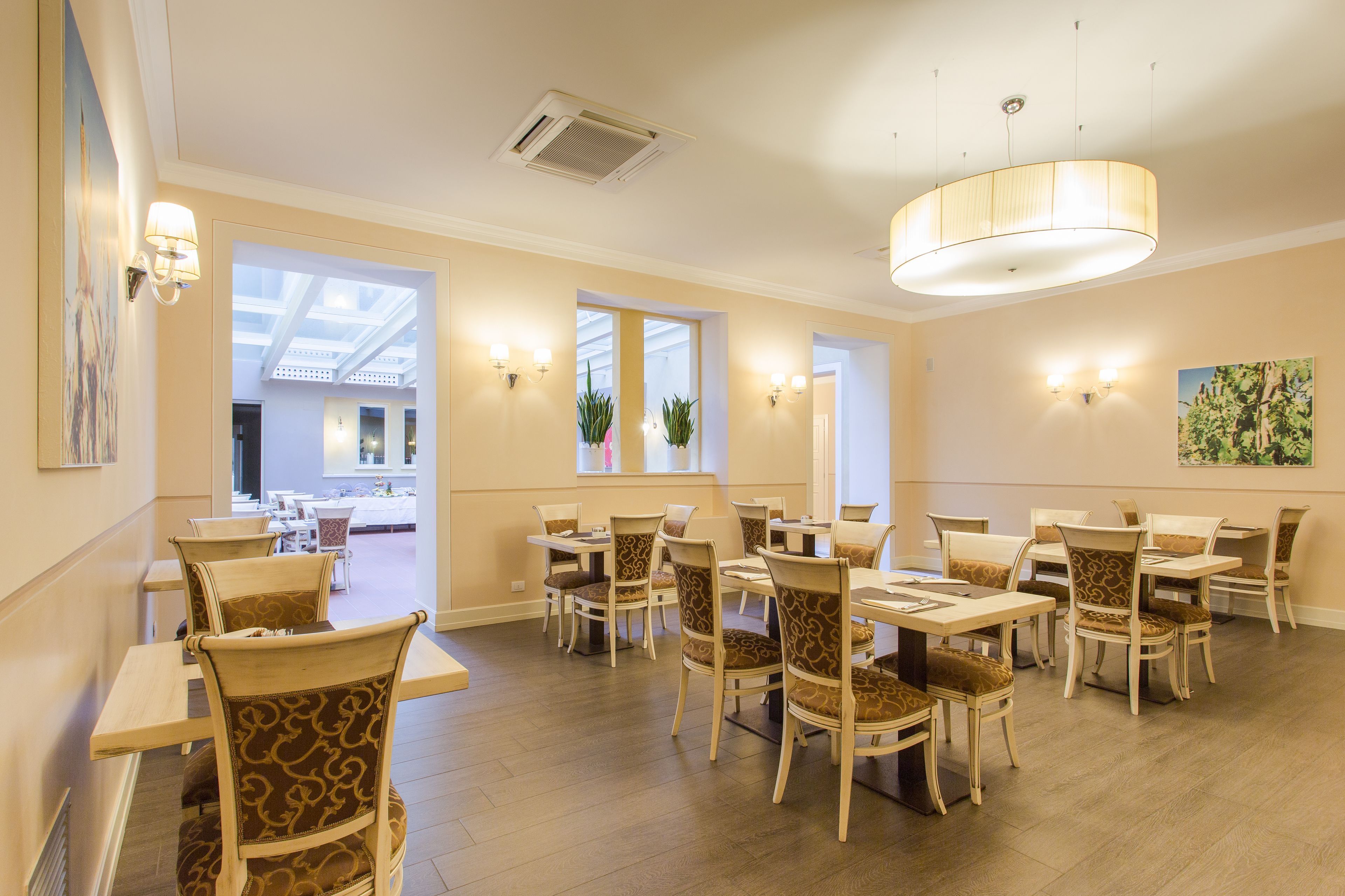 A dining area with multiple tables and chairs, large windows, and wall-mounted lighting.
