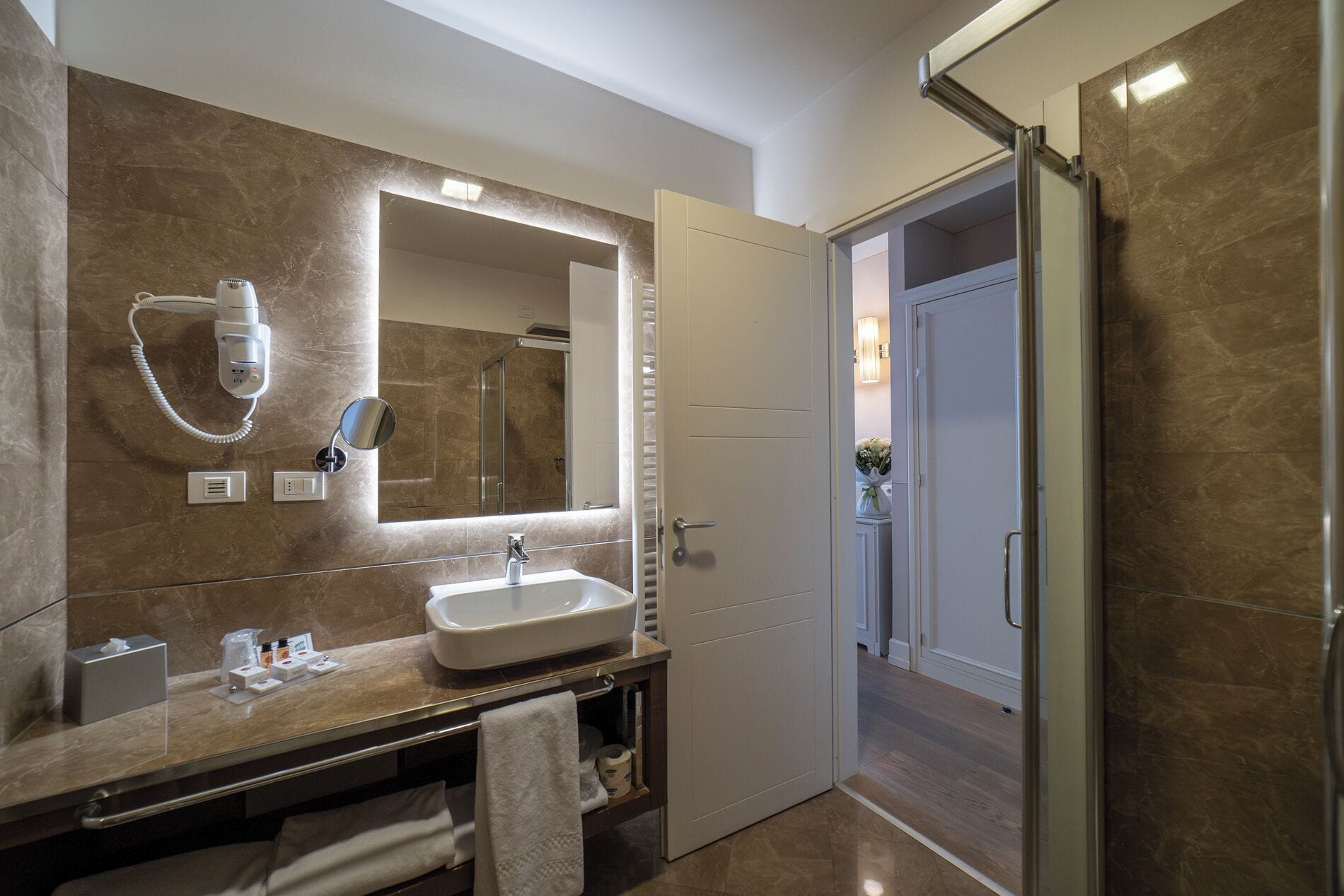 A modern bathroom with a large mirror, a sink, a hairdryer, and a shower area.