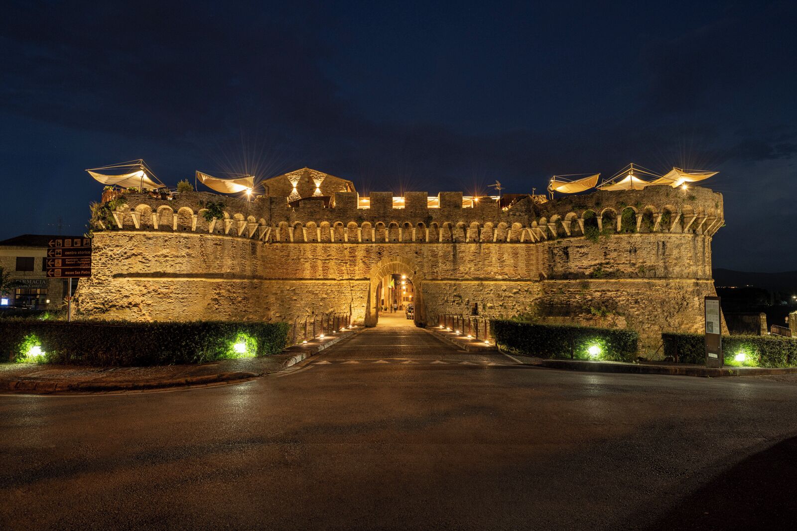 Un château de pierre historique, doté d’une entrée centrale, entouré de chemins bien éclairés et d’une route pavée devant.