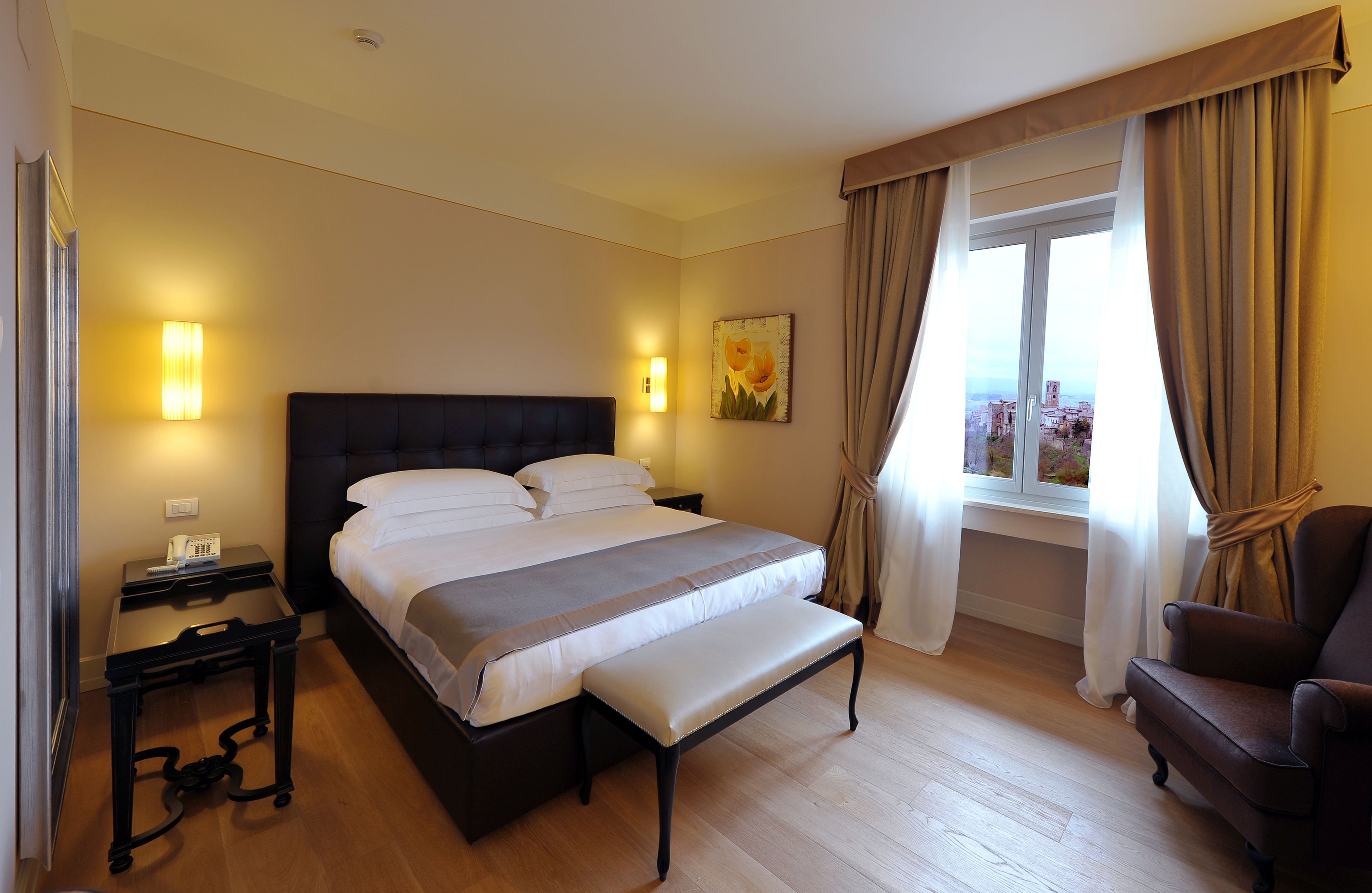 A hotel room with a large bed, bedside tables, a chair, and a window with curtains.