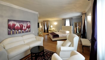 A hotel room with a bed, a sofa, a chair, a small table, and a painting on the wall.