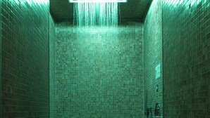 Zona de ducha con azulejos e iluminación cuadrada sobre el cabezal.