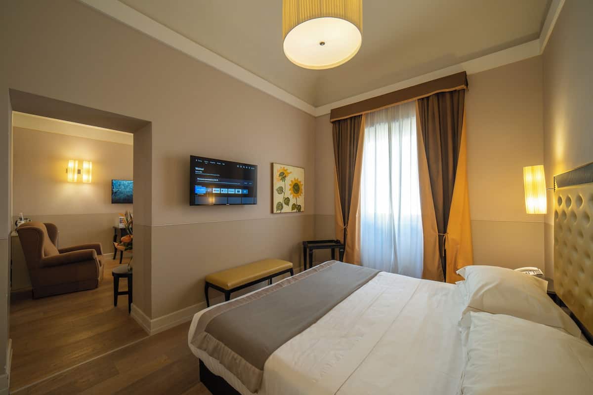 A hotel room with a bed, a desk, a chair, a TV, and a painting on the wall.