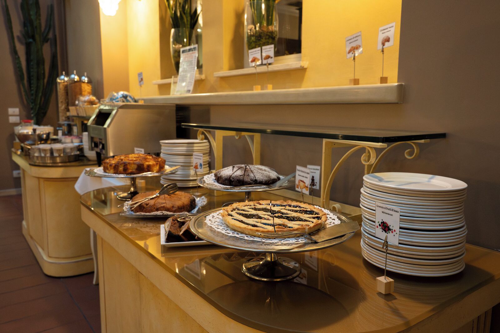 A buffet counter with various desserts displayed on trays, plates stacked on the side, and a sign indicating the dessert selection.