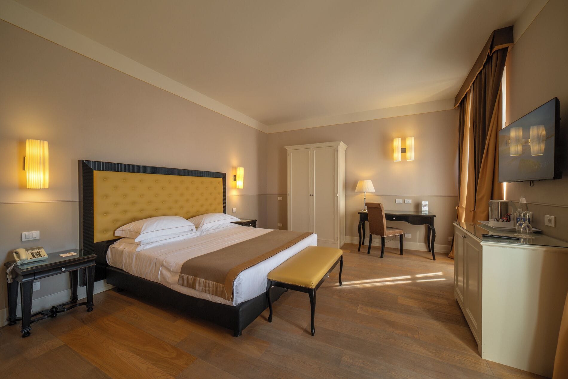 Habitación de hotel con una cama grande, mesitas de noche, escritorio, silla, banco, armario y televisor.