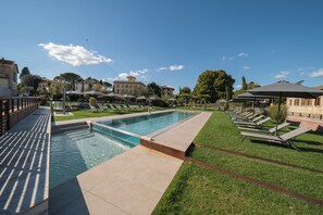 A swimming pool with a tiled deck, surrounded by grass and sun loungers.