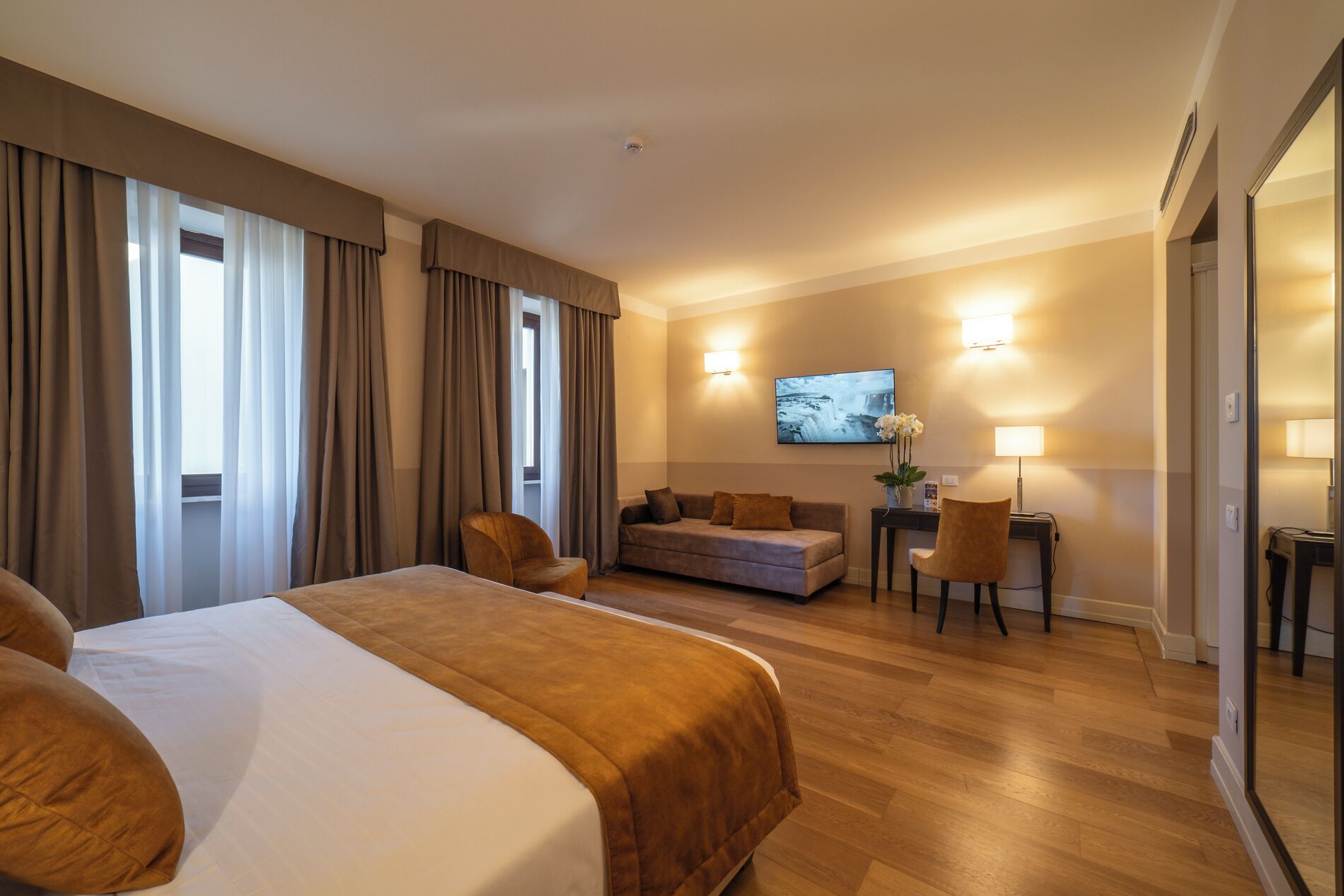 Habitación de hotel con una cama grande, un sofá, un escritorio con una silla y un televisor en la pared.