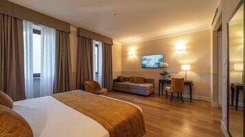 Habitación de hotel con una cama grande, un sofá, un escritorio con una silla y un televisor en la pared.