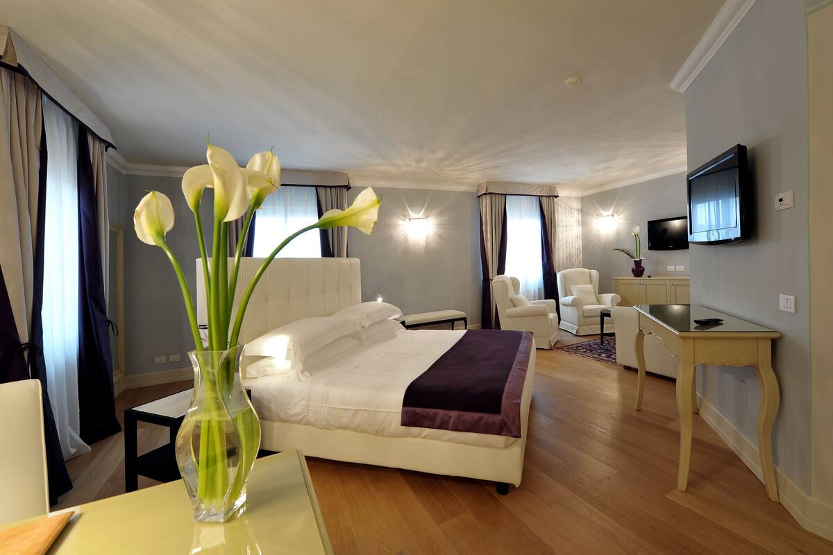 A hotel room with a bed, a desk, a chair, a TV, and a vase with flowers.