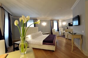 A hotel room with a bed, a desk, a chair, a TV, and a vase with flowers.