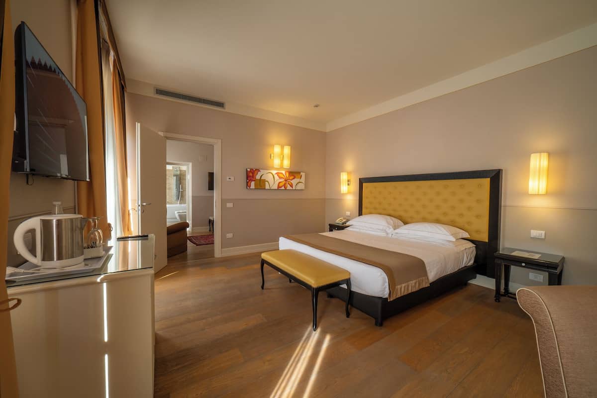 A hotel room with a bed, bedside tables, a desk with a kettle, and a television.