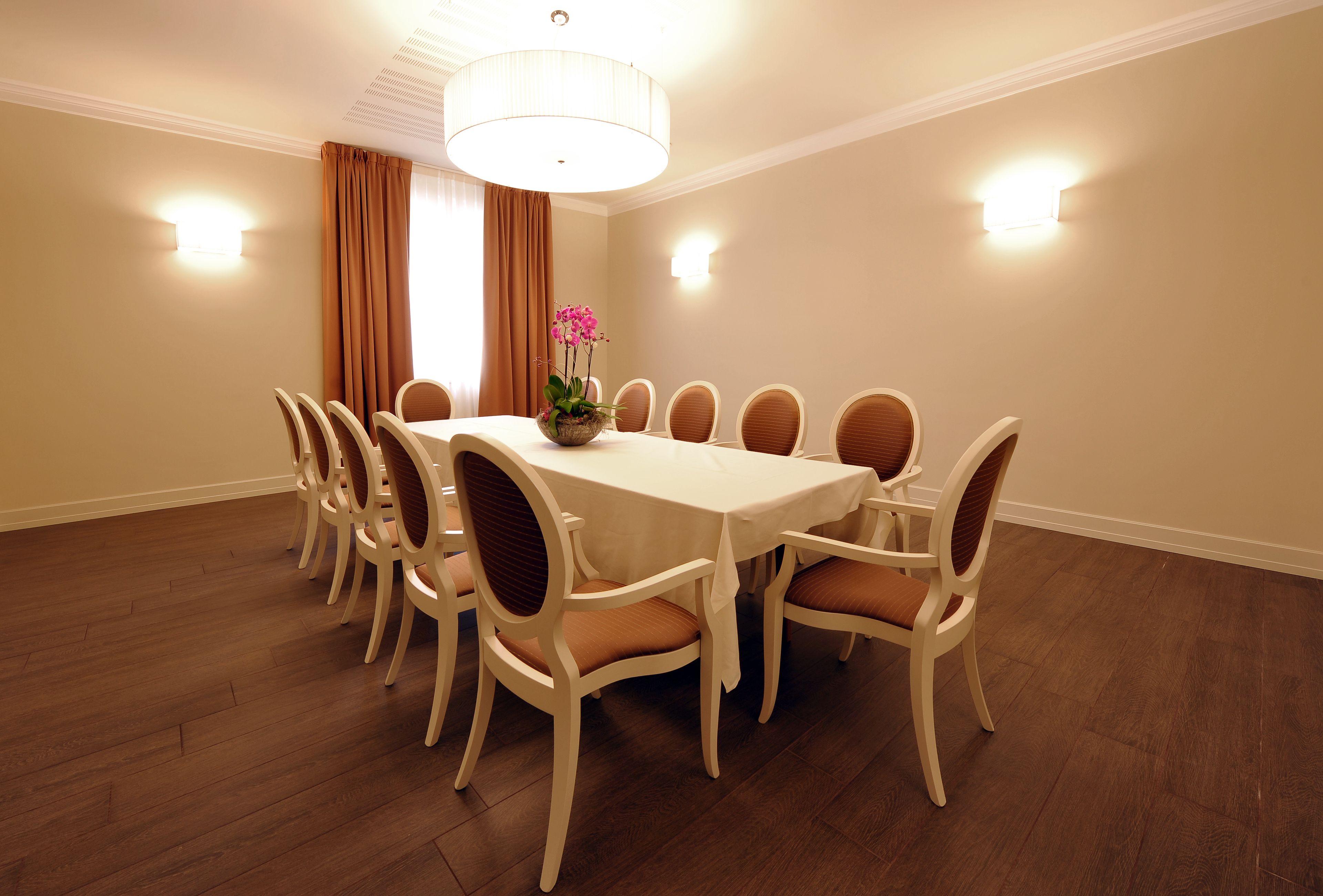 A dining room with a round table, eight chairs, a chandelier, and a vase with flowers.