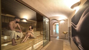 Un área de spa con bancos de madera y un separador de vidrio, un baño moderno con un lavamanos grande y un pasillo que conduce a otra habitación.