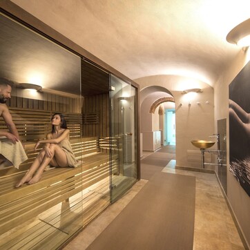 A spa area with wooden benches and a glass partition, a modern bathroom with a large sink, and a corridor leading to another room.
