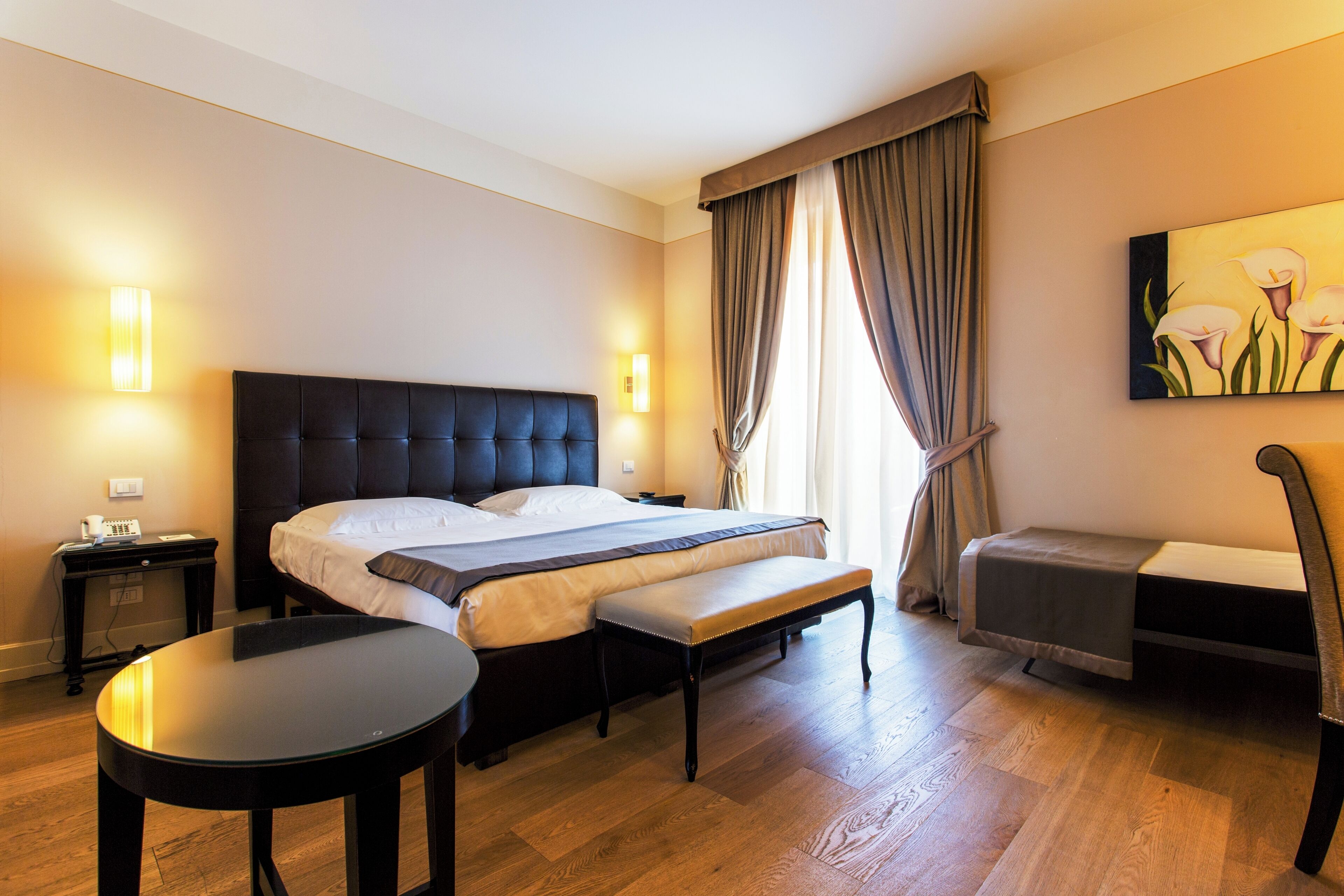 Habitación de hotel con cama, mesitas de noche, un banco, una pequeña mesa y un cuadro en la pared.