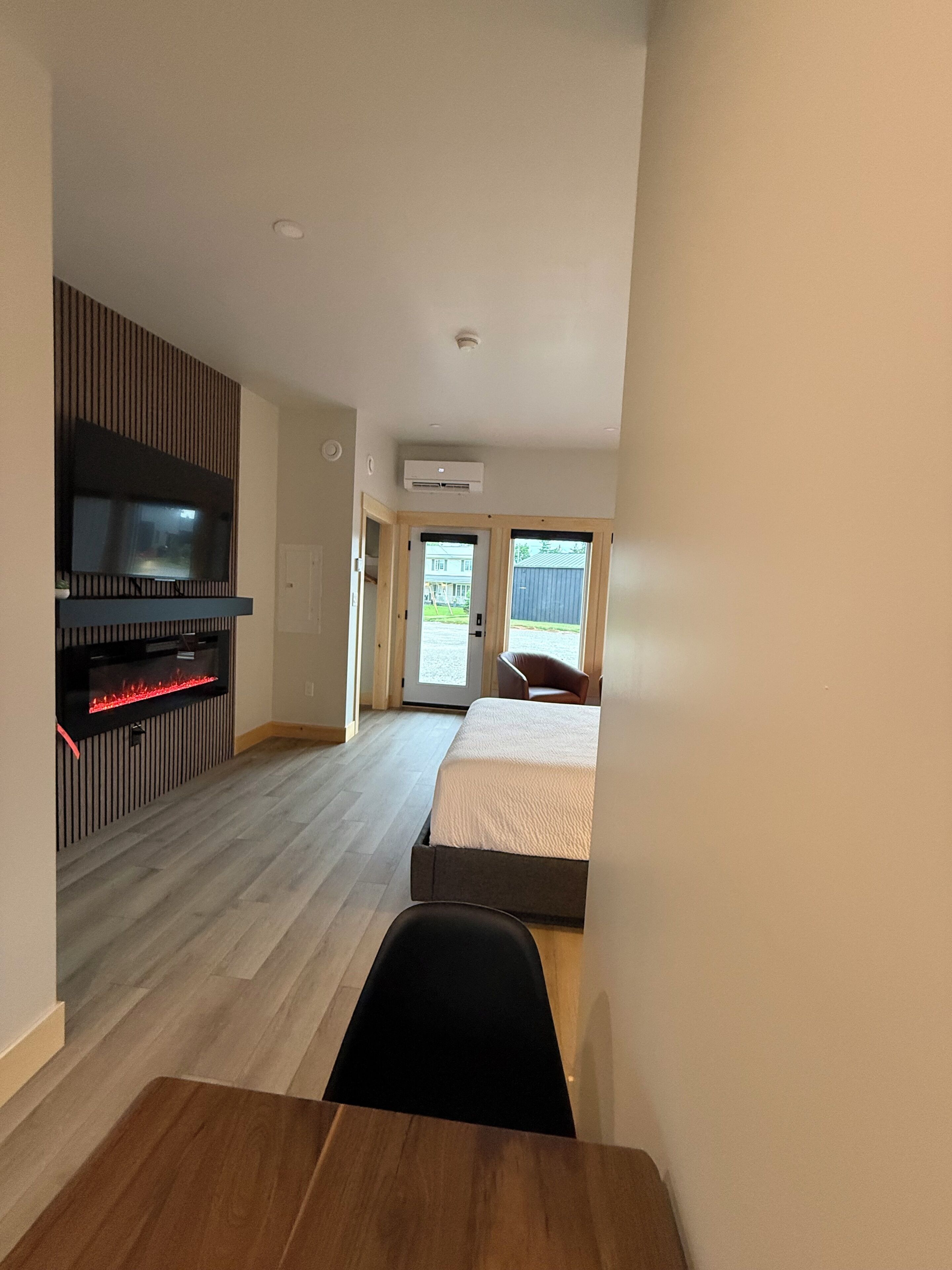A modern hotel room with a flat-screen TV, a fireplace, a bed, a desk, and a view of the outside.