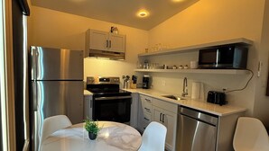 Cocina moderna con electrodomésticos de acero inoxidable, comedor con sillas blancas y una pequeña planta en maceta sobre la mesa.